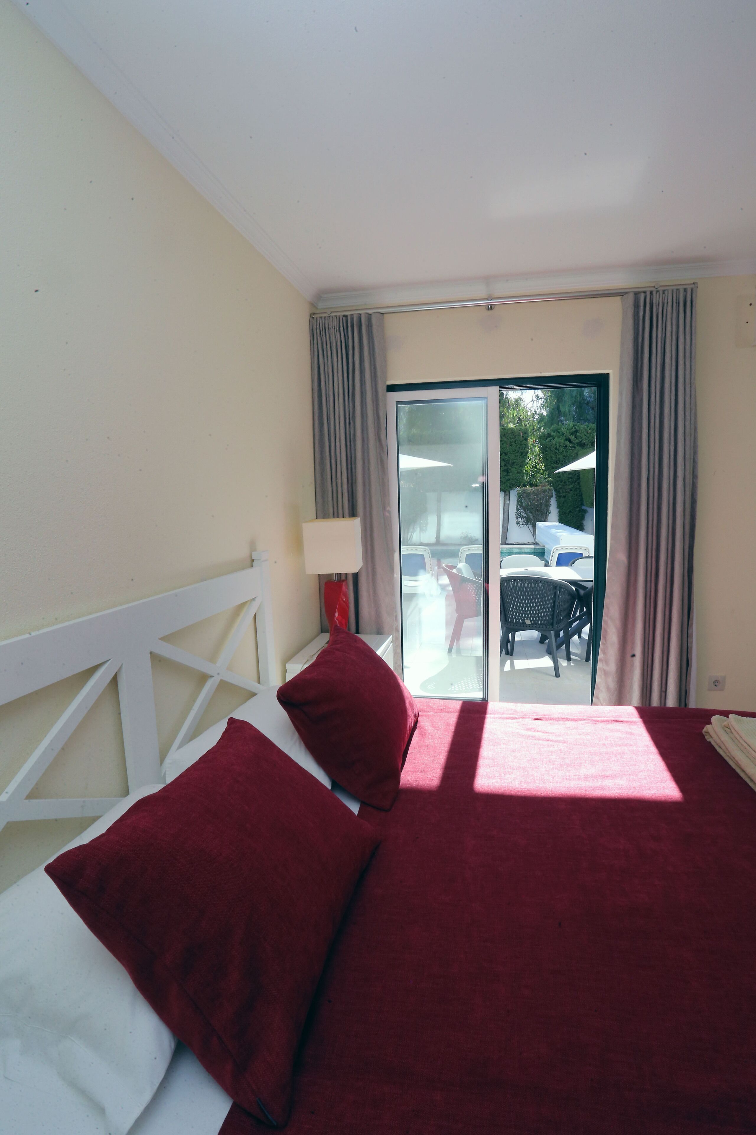 Ein Hotelzimmer mit Bett, Nachttisch, Lampe und Blick ins Freie.