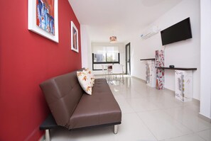 A modern living room with a brown sofa, a red accent wall, and a flat-screen TV mounted on the wall.