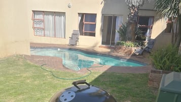 A barbecue grill with a lid and a side table, set on a grassy lawn with a pool in the background.