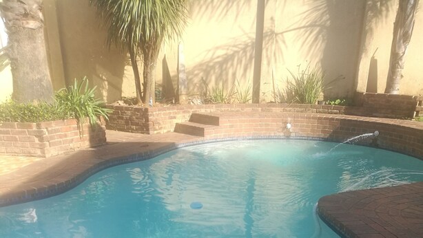 A swimming pool with clear blue water, surrounded by a brick border and a tiled edge. - Naisar Royal White Apartment (Germiston)