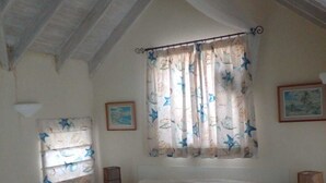 Een slaapkamer met een bed, een raam met gordijnen, een nachtkastje en een wandlamp.