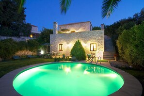 A stone building with a swimming pool, outdoor seating, and a well-lit patio area.