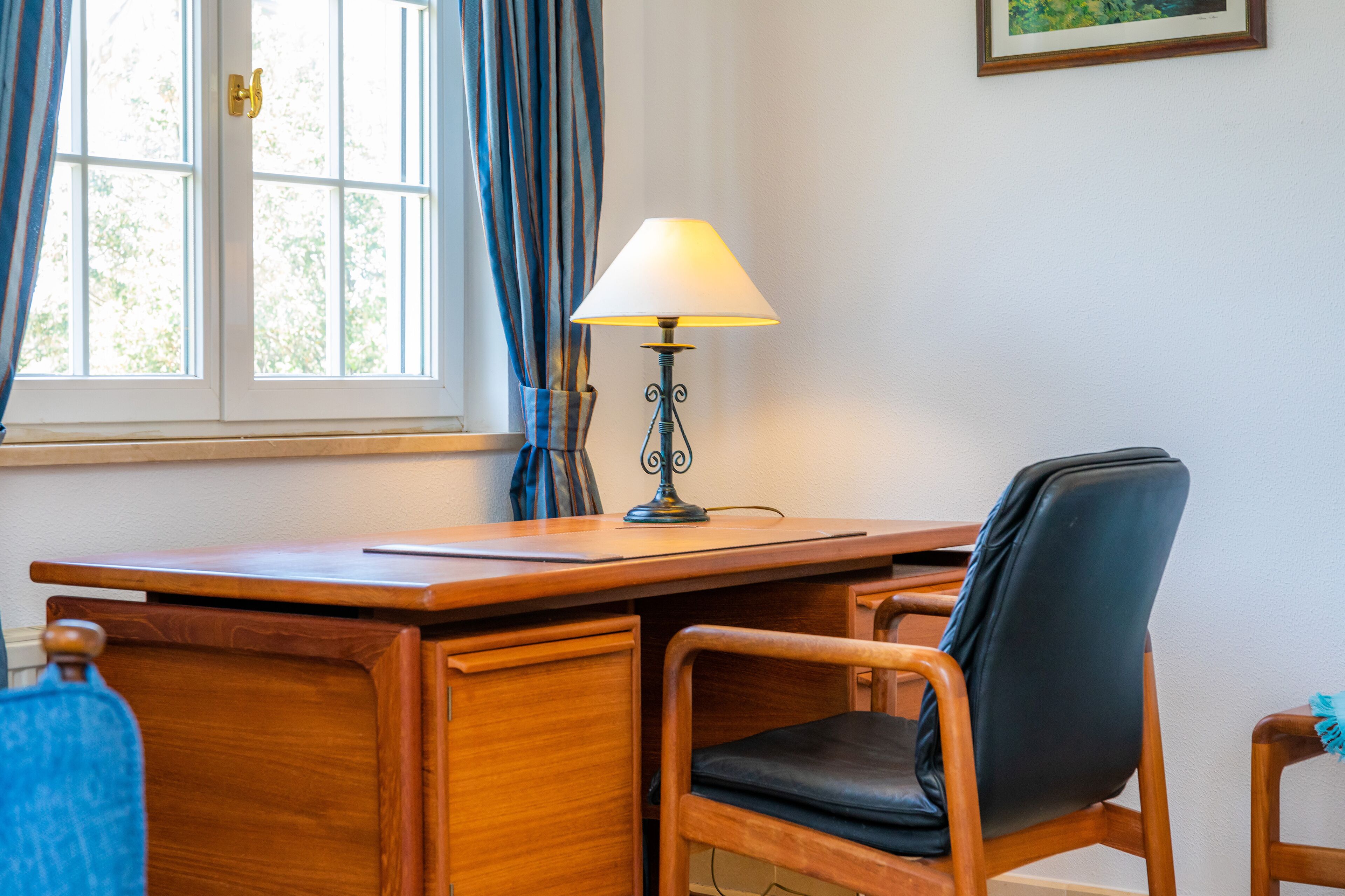 A wooden desk with a lamp, a chair, and a window with curtains.