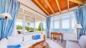A sunlit room with a wooden ceiling, large windows with blue curtains, a white sofa, a wooden table, and a view of the sea. - Finca by the sea (Colonia de Sant Pere)
