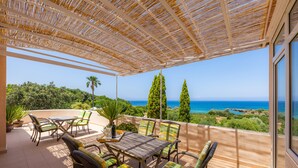 A covered outdoor patio with a table and chairs, overlooking a scenic view of the sea and greenery. - Finca by the sea (Colonia de Sant Pere)