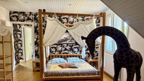 Un letto a baldacchino con tenda, una statua di giraffa e una stanza con carta da parati decorata.
