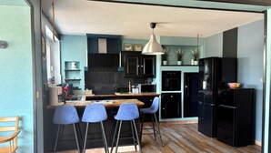 Una cucina moderna con isola centrale, sgabelli da bar, frigorifero nero e pavimento in legno.