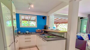 A compact kitchen with white cabinets, a white refrigerator, a window with blue walls, and a small dining area with a table and chairs.