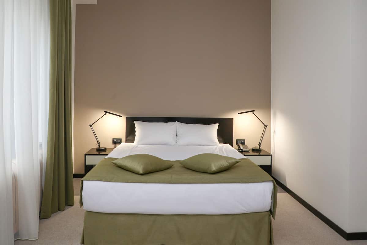 A hotel room with a large bed, two bedside tables with lamps, and green curtains.