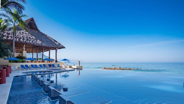 An infinity pool with a view of the ocean, lounge chairs, and a thatched-roof structure. - STUNNING 3 BR & 3BA SOUTH SHORE BEACHFRONT RESIDENCE! (Puerto Vallarta)