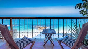 A balcony with two wooden lounge chairs and a small table, overlooking a beach with clear blue waters and rocky outcrops. - STUNNING 3 BR & 3BA SOUTH SHORE BEACHFRONT RESIDENCE! (Puerto Vallarta)