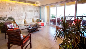 A spacious living area with a stone wall, a sofa set, a coffee table, and a view of the outdoors through large sliding doors. - STUNNING 3 BR & 3BA SOUTH SHORE BEACHFRONT RESIDENCE! (Puerto Vallarta)