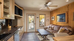 A kitchen with wooden cabinets, a countertop, and a ceiling fan. There is a door leading to a balcony with a view of trees and a house.