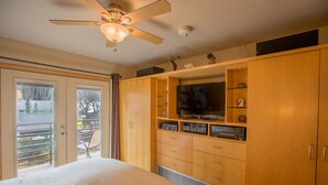 A bedroom with a bed, a ceiling fan, a television, and a wooden wardrobe.