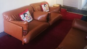 A brown leather sofa with decorative pillows, a red carpet, and a white door in the background. - Naisar Sparkling White Apartment (Germiston)