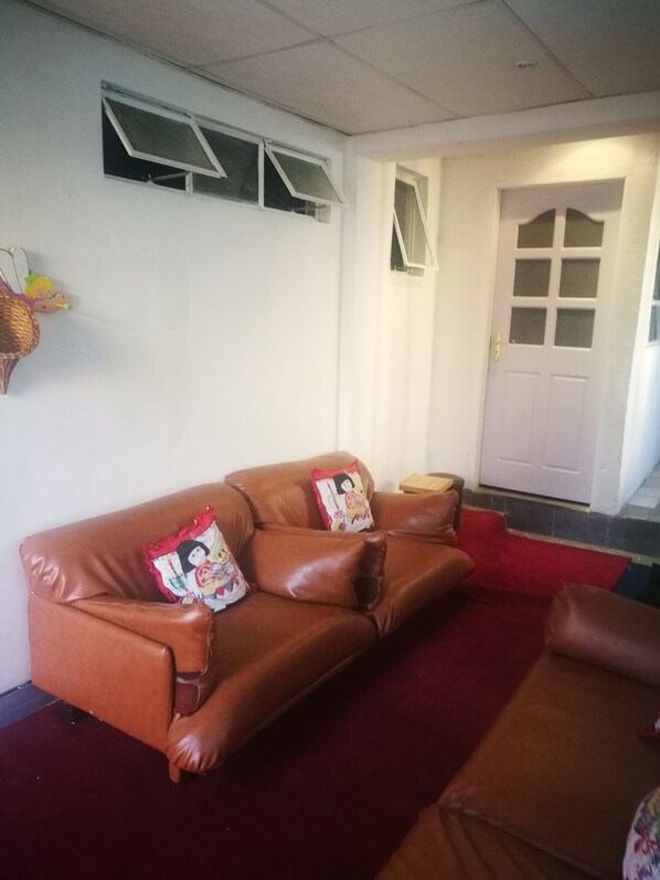 A brown leather sofa with decorative pillows, a red carpet, and a white door in the background. - Naisar Sparkling White Apartment (Germiston)