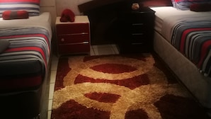 A bedroom with two beds, a red and white striped rug, and a small red object on a nightstand. - Naisar Sparkling White Apartment (Germiston)