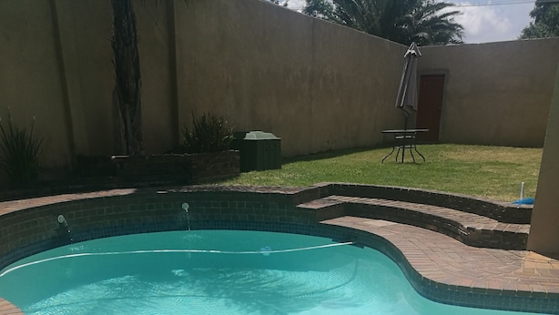 A swimming pool with a curved edge, surrounded by a brick patio. - Naisar Sparkling White Apartment (Germiston)