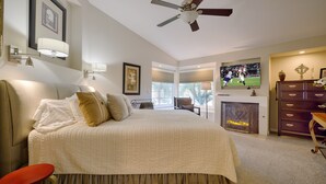 Een slaapkamer met een groot bed, een plafondventilator, een televisie, een open haard en een dressoir.