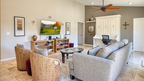 Een woonkamer met een grijze bank, rieten stoelen, een glazen salontafel en een televisie.