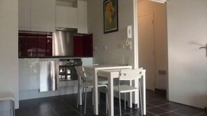 A compact kitchen with white cabinets, a stainless steel range hood, and a small dining table with two chairs.