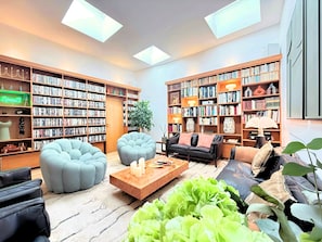 Eine moderne Bibliothek mit hohen Decken, Oberlichtern und großen Bücherregalen voller Bücher. Bequeme Sitzbereiche mit Sofas und einem Couchtisch.