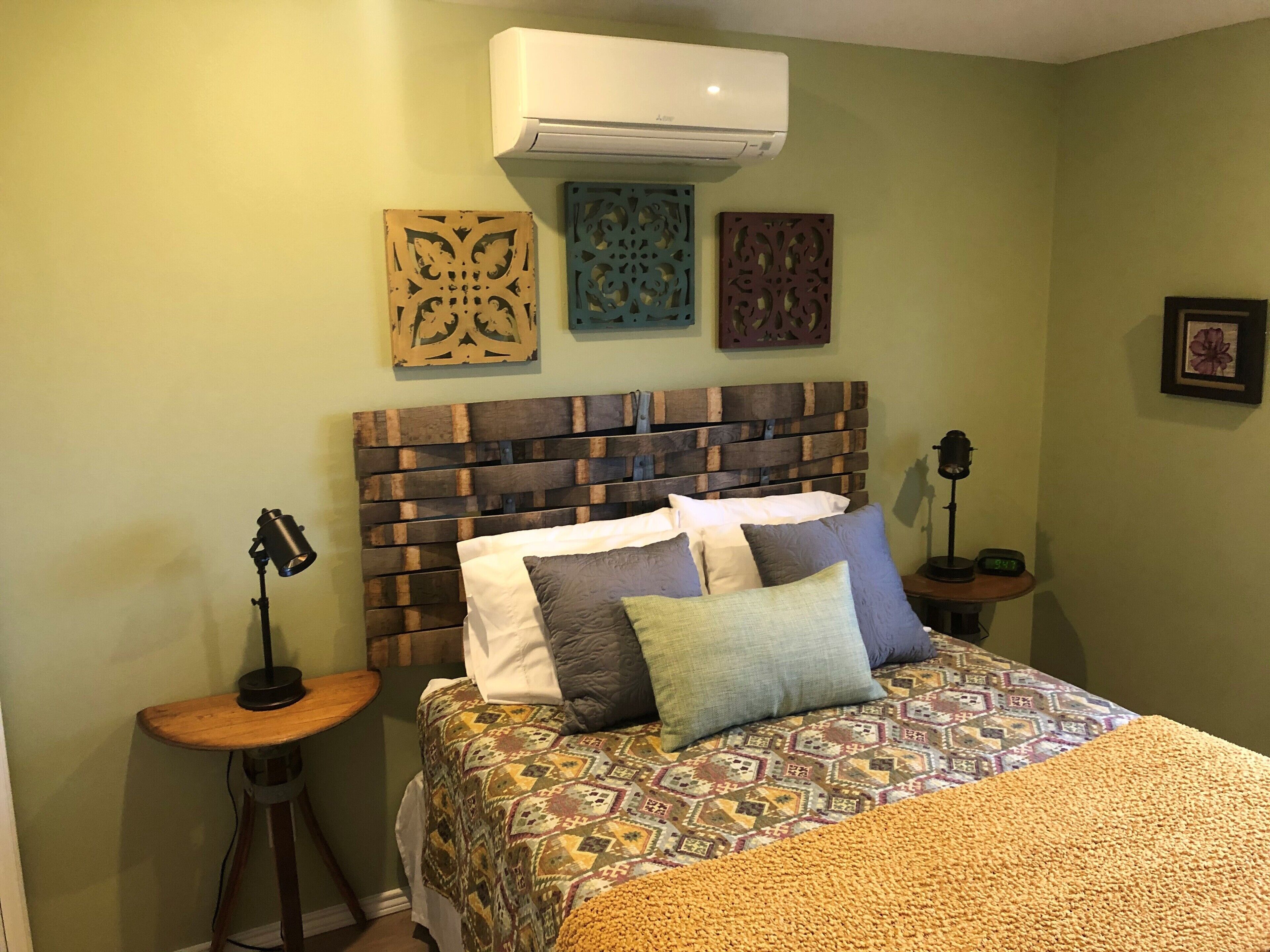 Une chambre à coucher avec une tête de lit en bois, une literie à motifs et des œuvres d’art décoratives accrochées au mur.