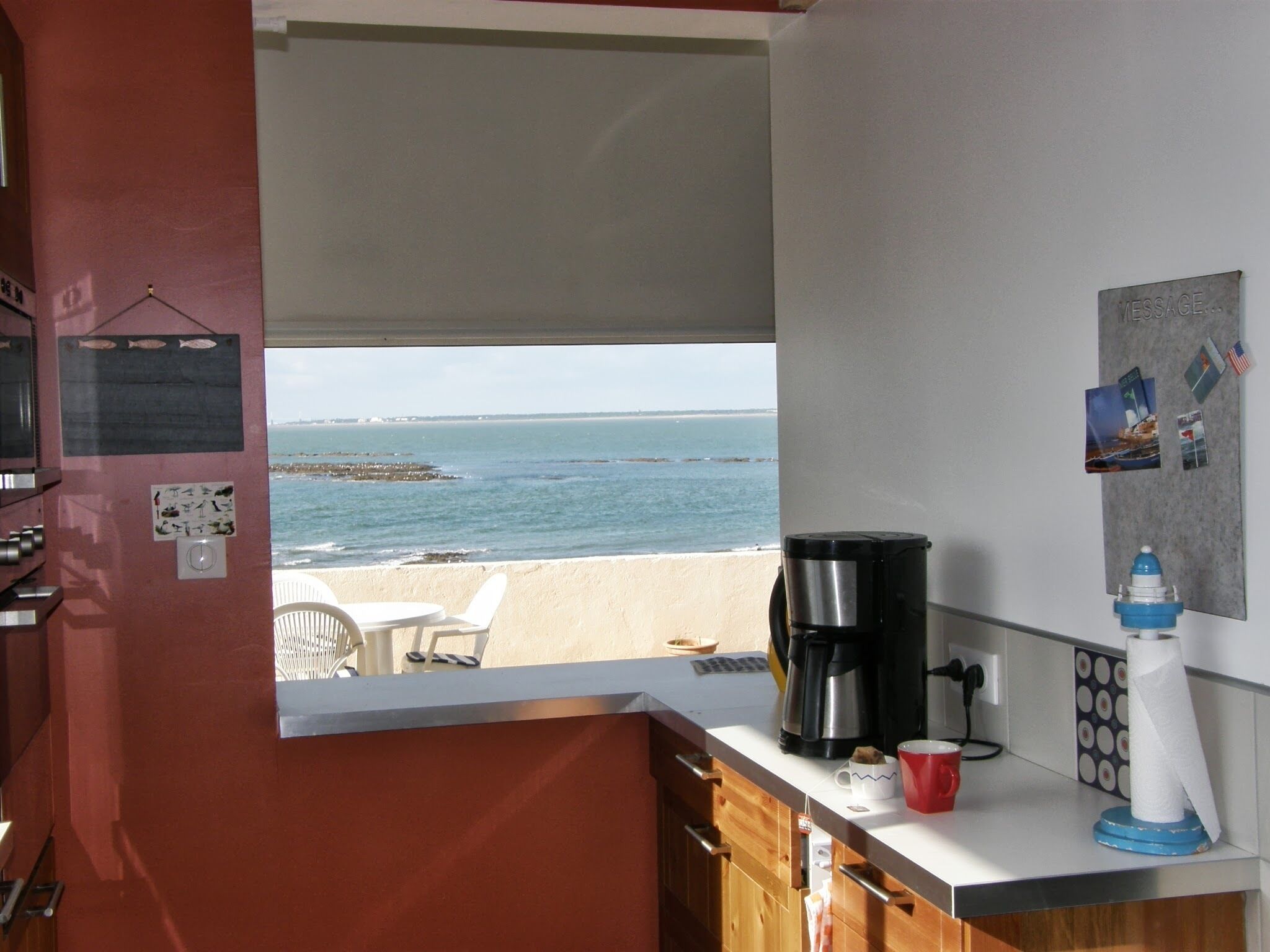 Une cuisine avec vue sur la plage, une machine à café et un tableau d’affichage où sont accrochées des photos.