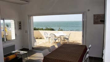 Een kamer met een tafel en stoelen, gericht op een balkon met uitzicht op zee.