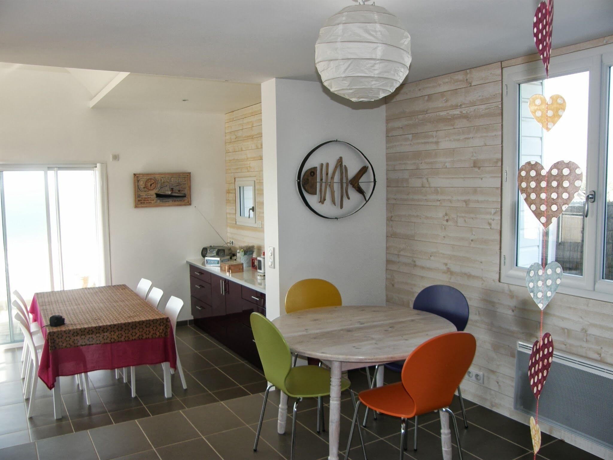 Un comedor con una mesa y sillas, una cocina al fondo, y una pared con un reloj y una decoración de pez.