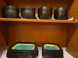 Un ensemble de bols noirs posés sur une étagère et une pile d’assiettes noires avec un motif turquoise au centre.