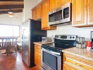 Una cocina con gabinetes de madera, un refrigerador de acero inoxidable, un microondas, un horno y una cafetera.