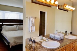 Quarto com cama, banheiro com duas pias, espelho e toucador.