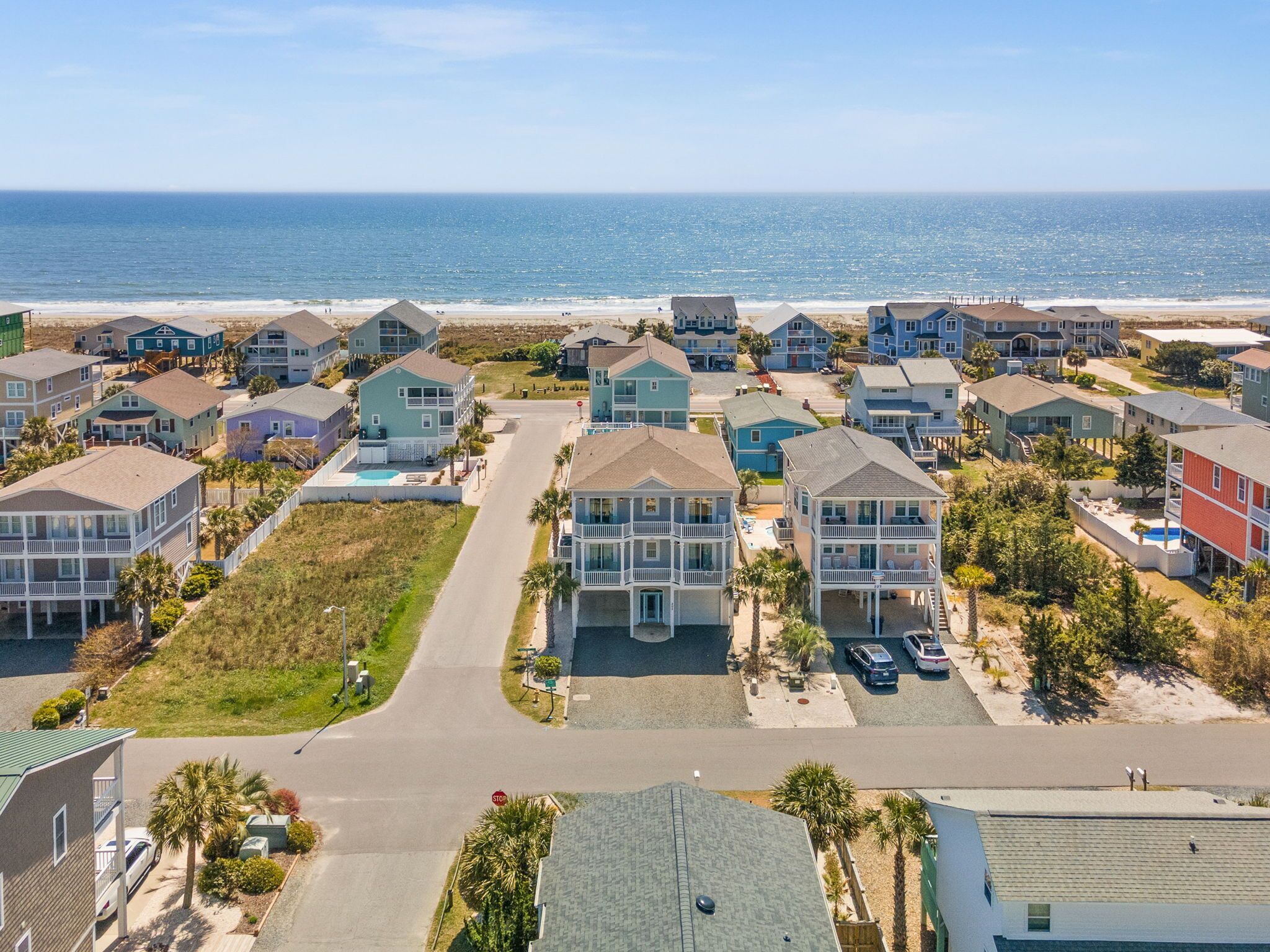 A coastal residential area with multiple two-story houses, a central road, and a beach in the background.