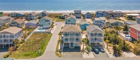A coastal residential area with multiple two-story houses, a central road, and a beach in the background.