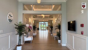 A spacious hallway with a high ceiling, wooden flooring, and a seating area with white sofas and potted plants. - Ocean Front Community- Ocean Village at South Hutchinson Island- Treasure Coast (Fort Pierce)