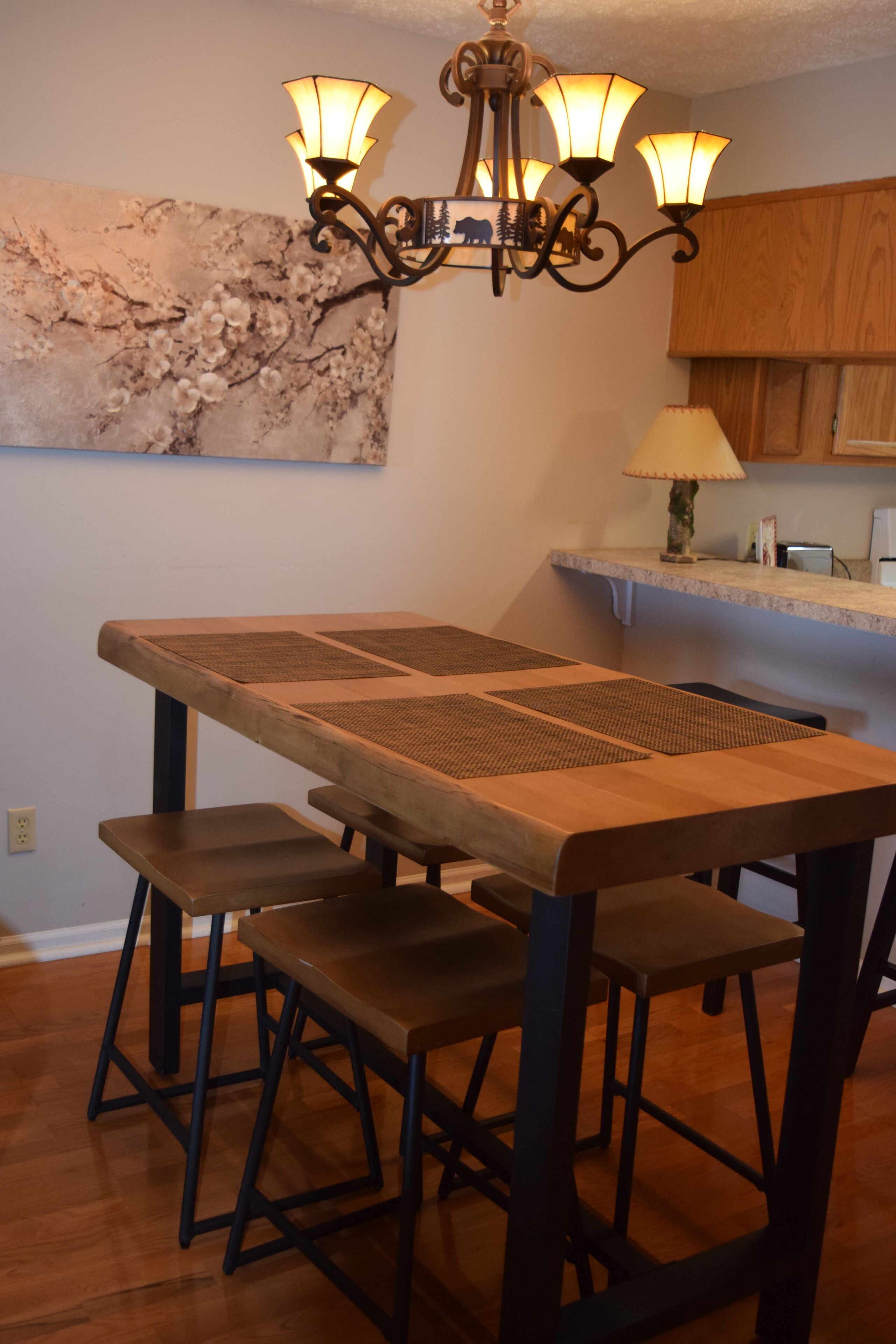 Un comedor con una mesa y bancos de madera, una araña y una encimera de cocina con una lámpara.