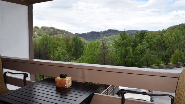 A balcony with a table and chairs, overlooking a forested valley.