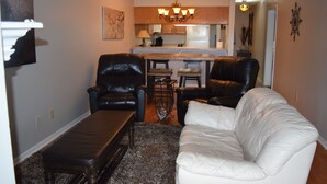 A living room with a white sofa, two black leather chairs, a coffee table, and a rug.