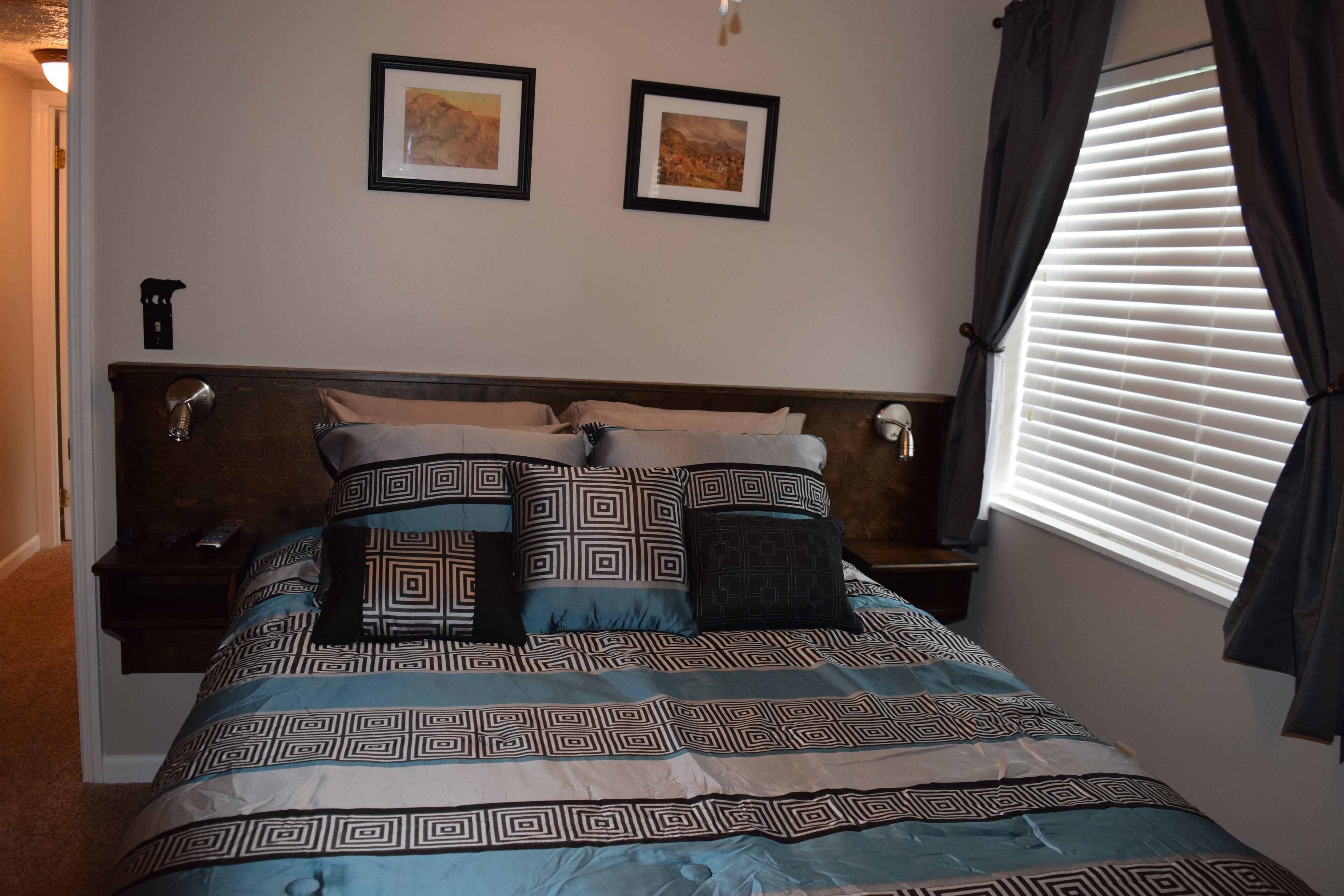 A neatly made bed with patterned bedding, a headboard, and two framed pictures on the wall.