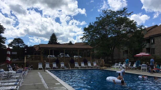 Una piscina con sillones de descanso y sombrillas, rodeada de árboles y edificios.