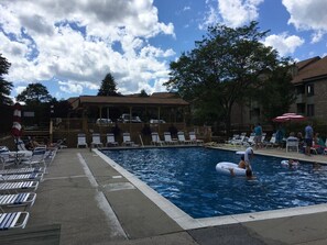 Une piscine entourée d’arbres et de bâtiments, avec des chaises longues et des parasols.