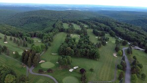 Vista aérea de un campo de golf con varios hoyos, rodeado de bosques densos y colinas.