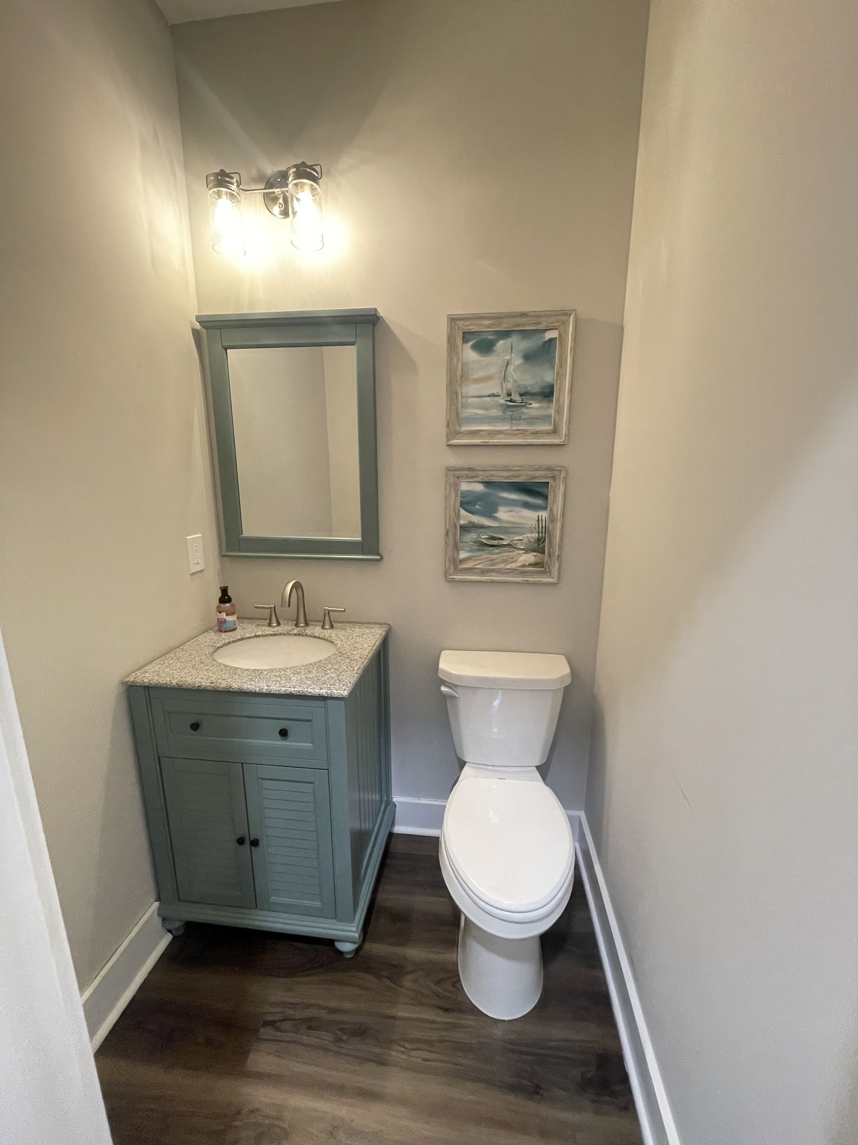 A bathroom with a sink, mirror, toilet, and two framed pictures on the wall.