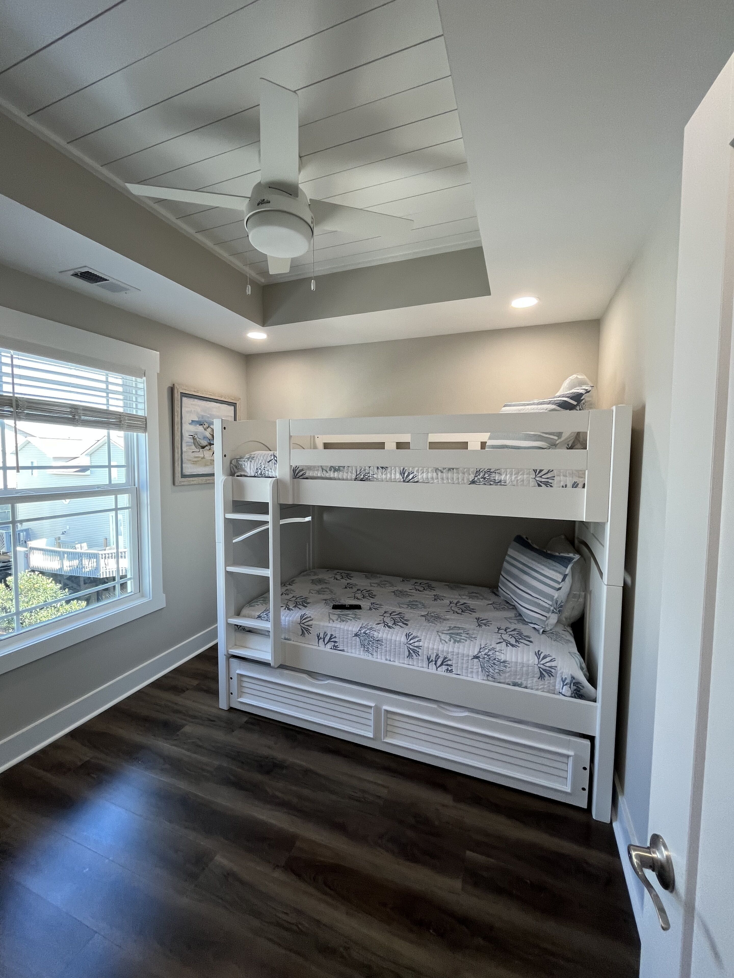 A bunk bed room with a ceiling fan, a window with blinds, and a door.