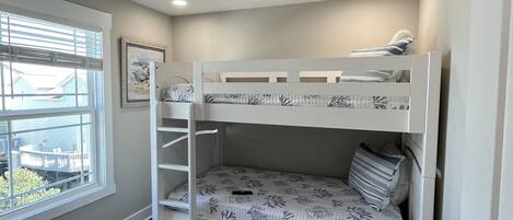 A bunk bed room with a ceiling fan, a window with blinds, and a door.