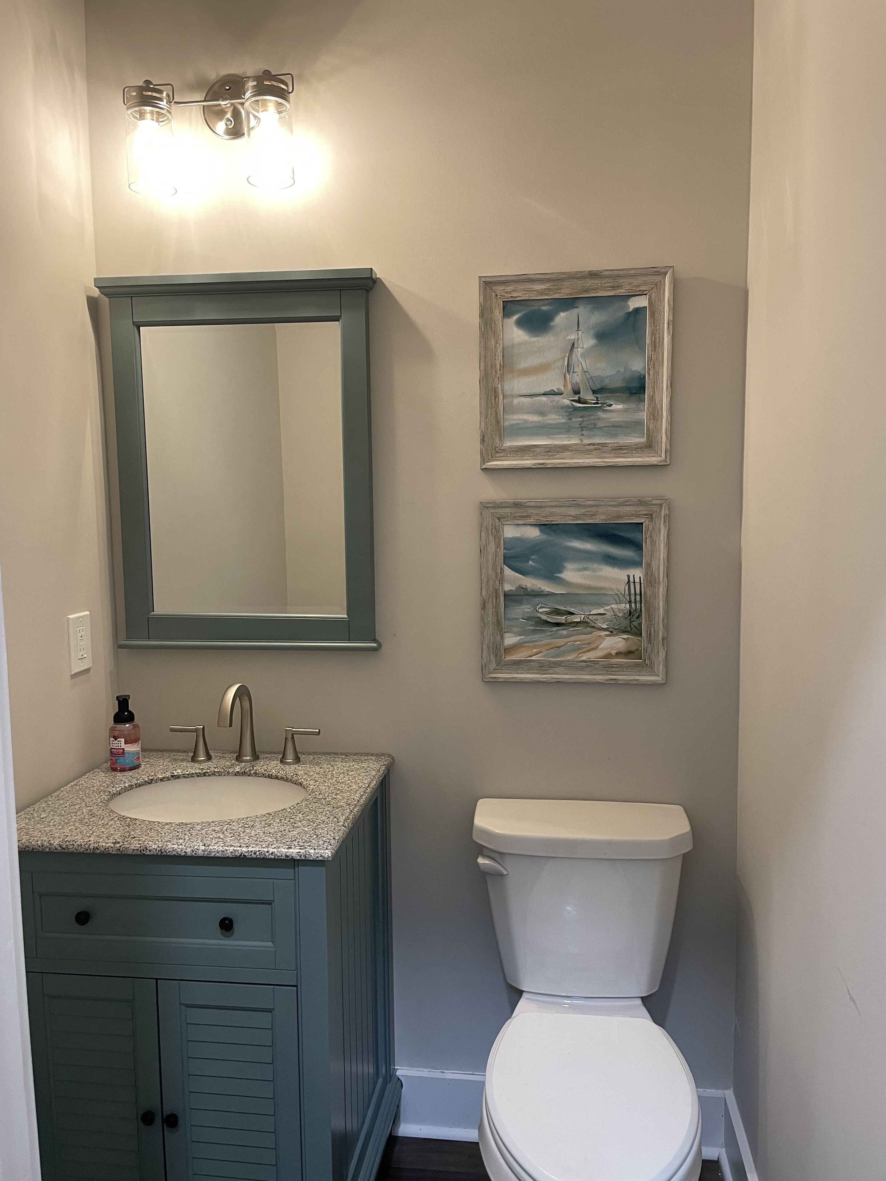 A bathroom with a sink, mirror, and toilet. There are two framed paintings on the wall.