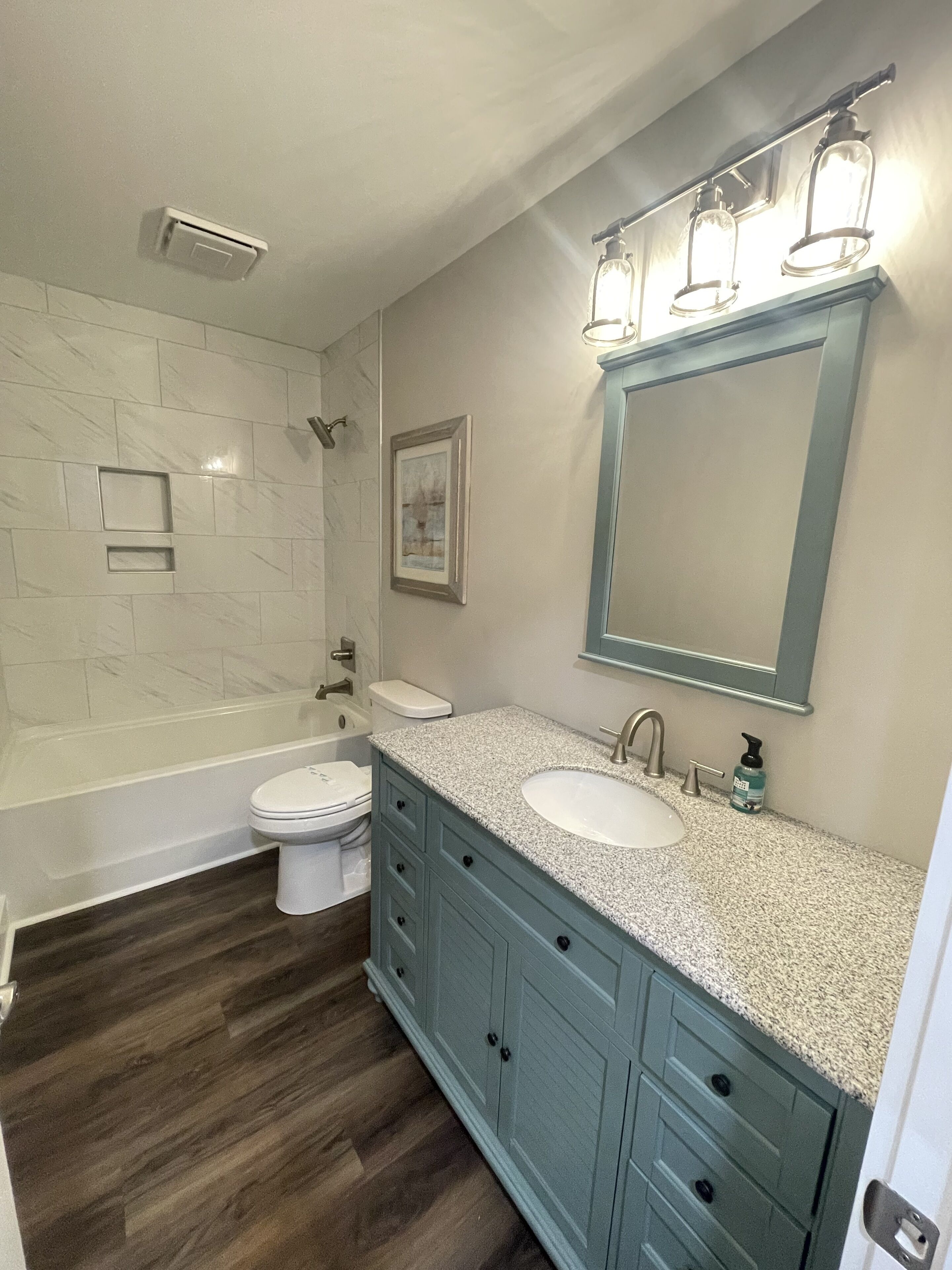 A bathroom with a bathtub, toilet, sink, vanity, and a framed picture on the wall.