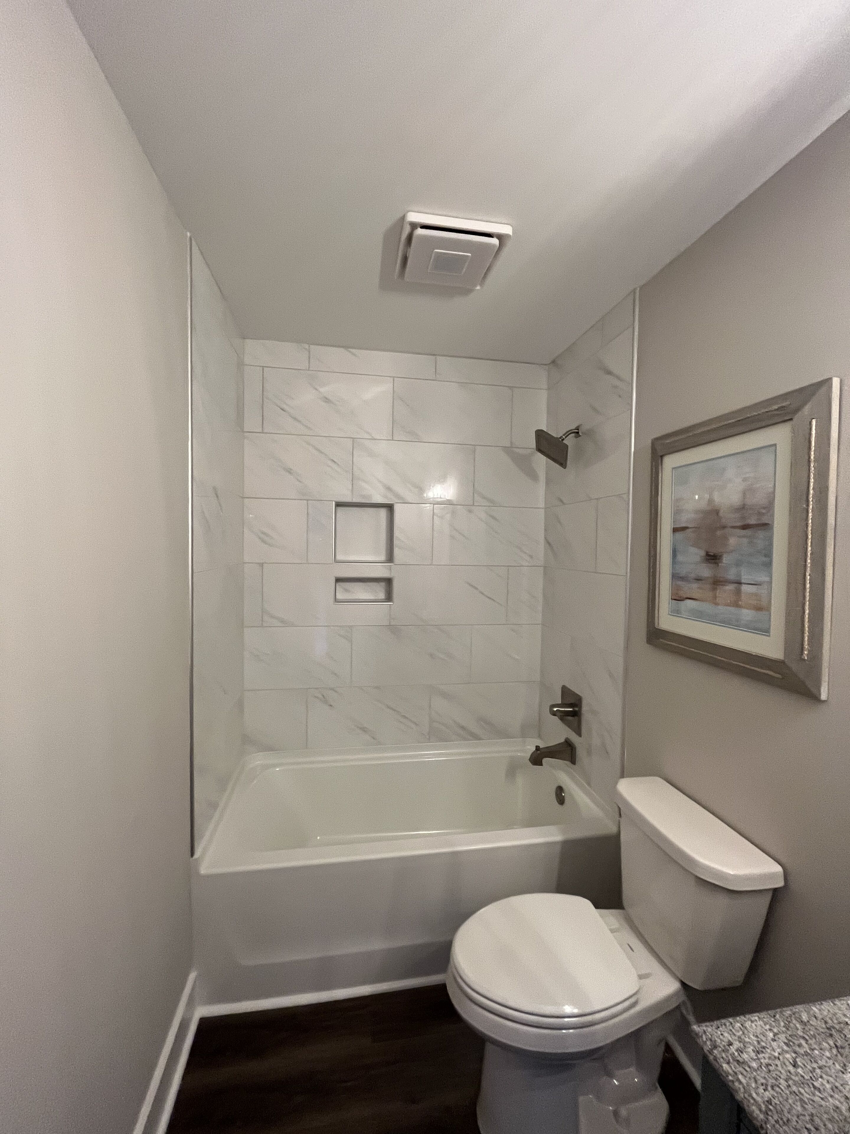 A bathroom with a bathtub, toilet, and a framed picture on the wall.