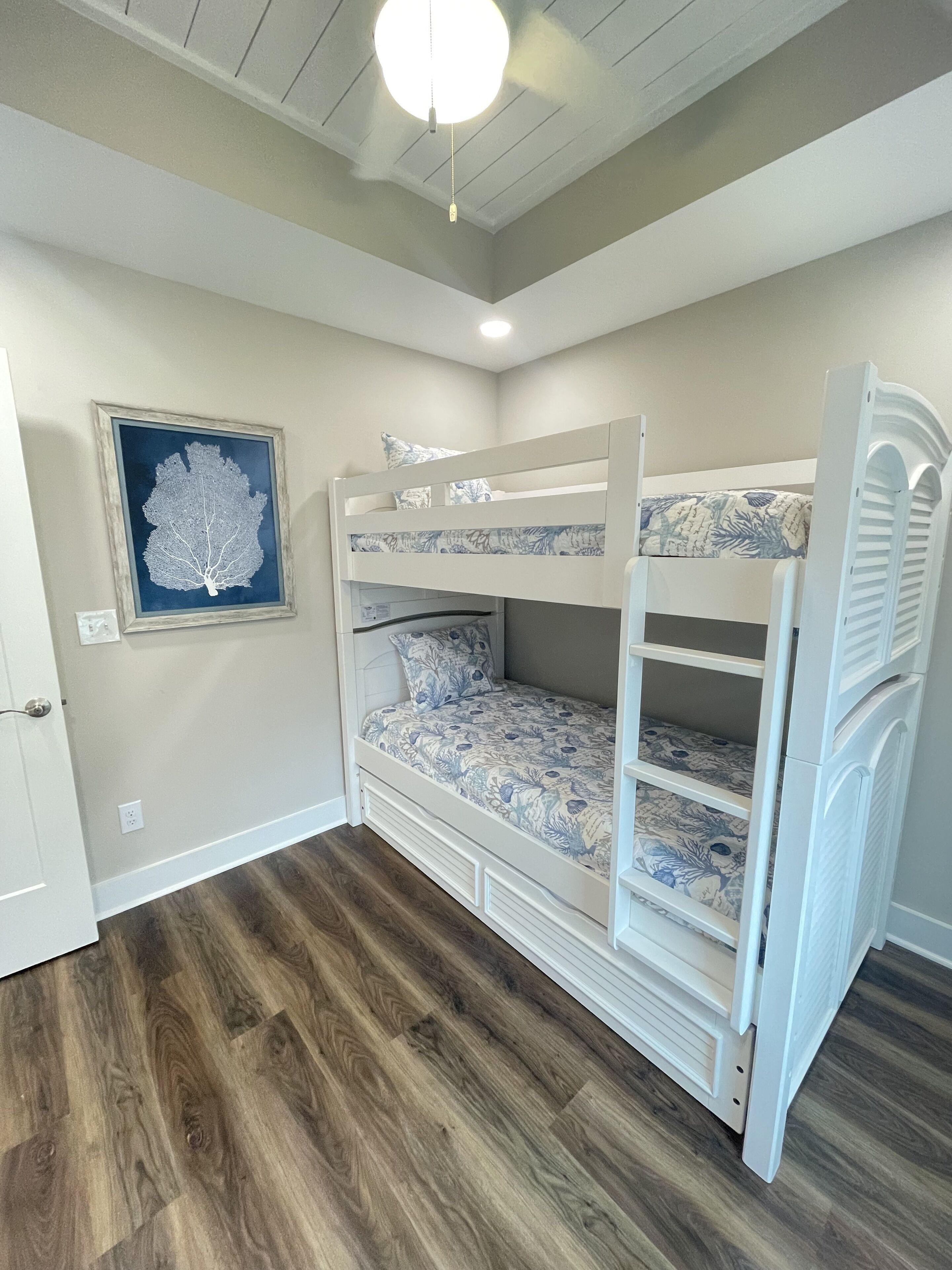 A bunk bed room with a ceiling fan, a framed leaf artwork, and a door.